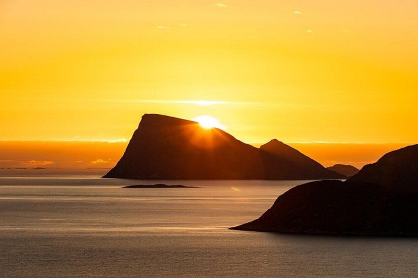 A sunset over a calm sea with a prominent mountain in the foreground and a smaller mountain in the background. 2