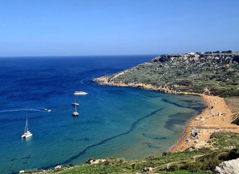 A coastal landscape with clear blue waters, a sandy beach, and rocky cliffs. 1
