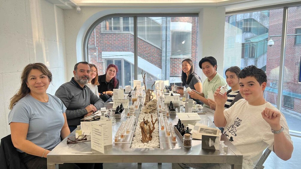 A group of people seated around a table with various items, including bottles and a decorative centerpiece, in a room with large windows and brick walls. 3