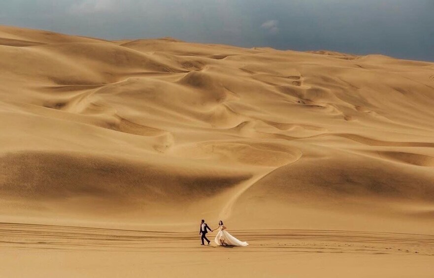 A couple walking on a sand dune in a desert landscape. 1