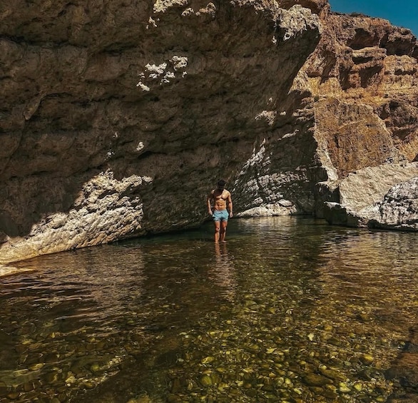 A person standing in a clear water body surrounded by rocky terrain. 5
