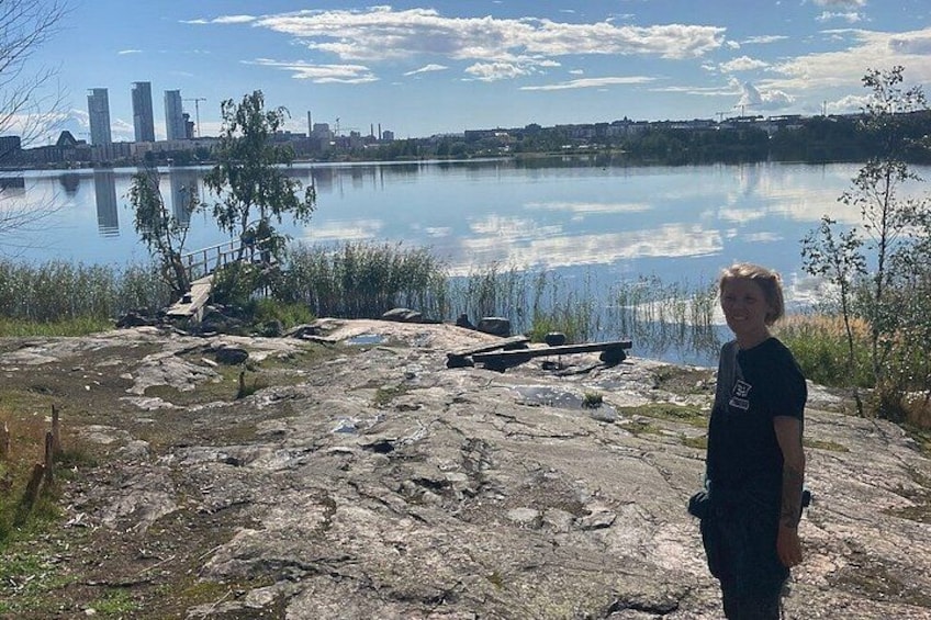 A rocky shoreline with a person standing, a calm lake, and a city skyline in the background. 2