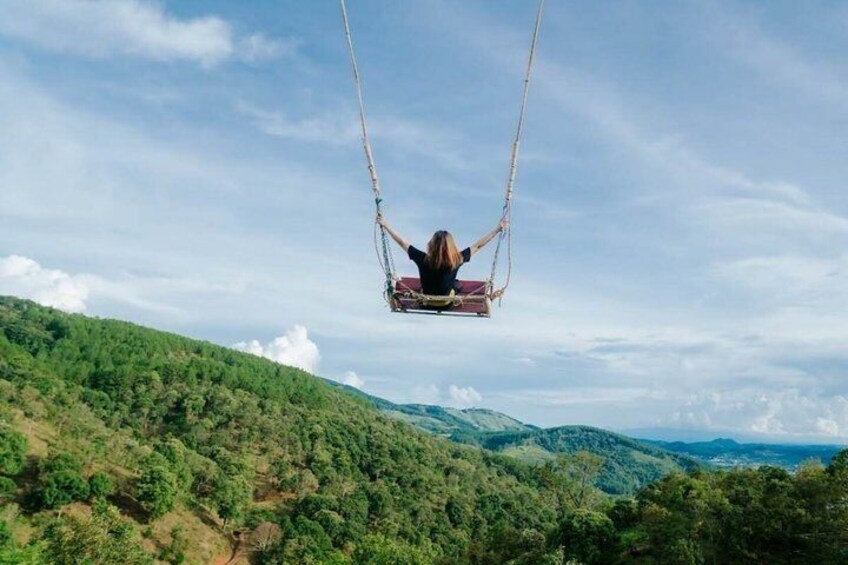 A person on a swing chair suspended by ropes, overlooking a hilly landscape with dense vegetation. 5