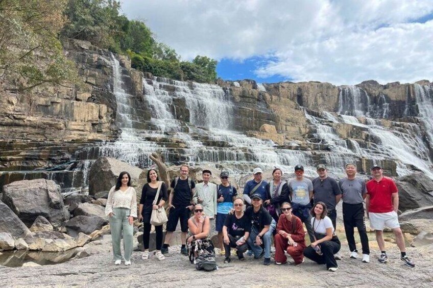 A group of people posing in front of a multi-tiered waterfall with rocky terrain. 4