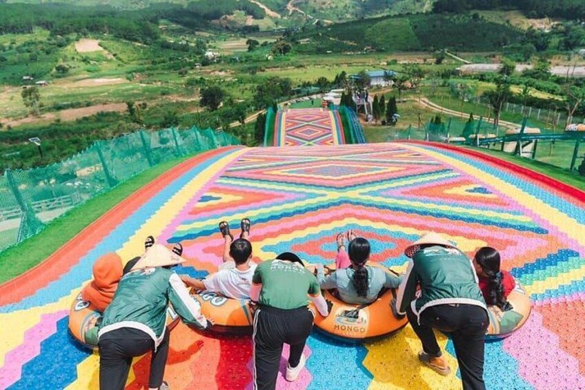A colorful slide with people at the bottom, a patterned carpet, and a green landscape in the background. 1