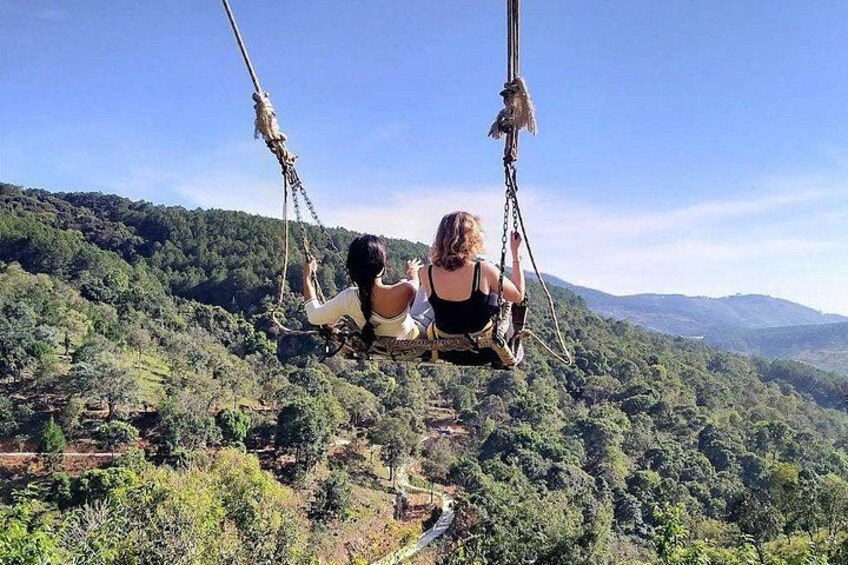 Two people on a swing overlooking a forested valley. 5