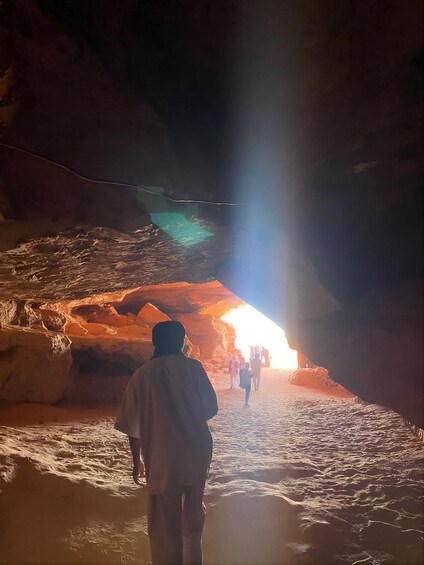 A cave with a bright light at the end of a passage, people walking towards it, and rocky walls. 4