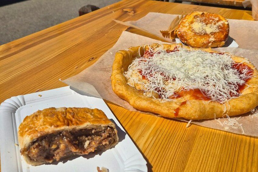 Een houten tafel met drie soorten eten: een pizza met kaas en tomatensaus, een gebakje met een goudbruine korst, en een gedeeltelijk opgegeten taart met een bladerdeegkorst. 5