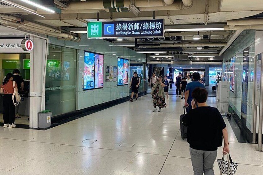 A subway station with people walking, digital advertisements, and an exit sign. 2