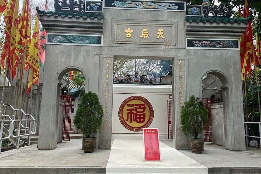 A traditional Chinese gate with a circular emblem, two potted plants, and a red sign with Chinese characters. 1