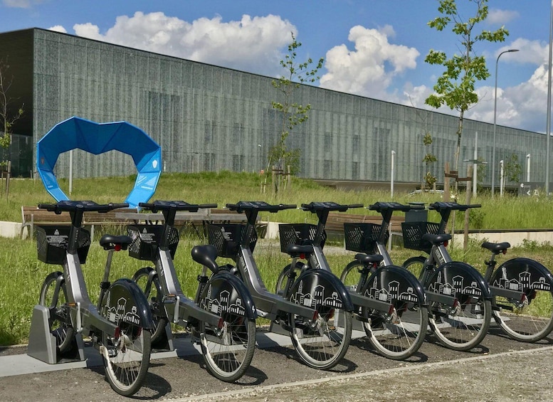 A row of electric bicycles parked in a bike-sharing station with a modern building in the background. 5