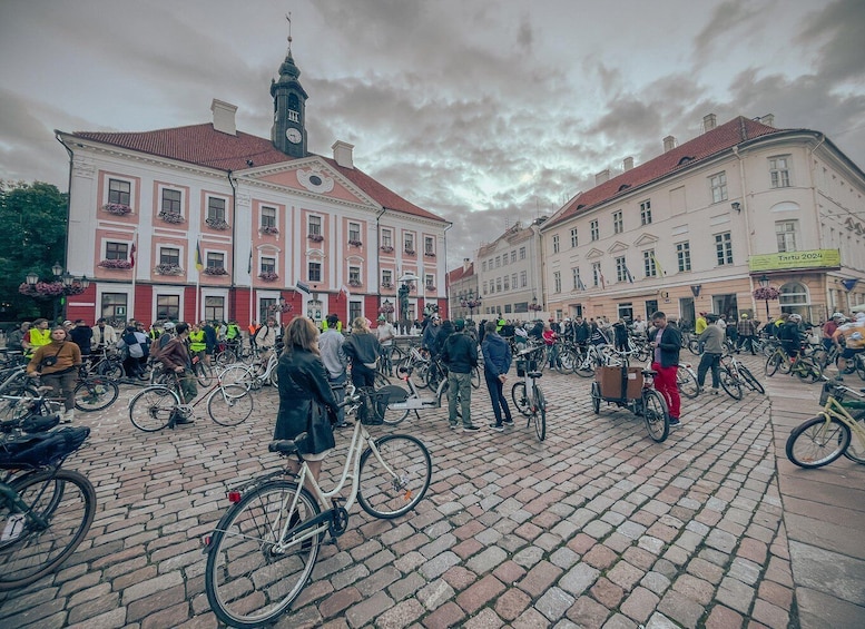 A crowded public square with people and bicycles, historic buildings, and a clock tower. 3