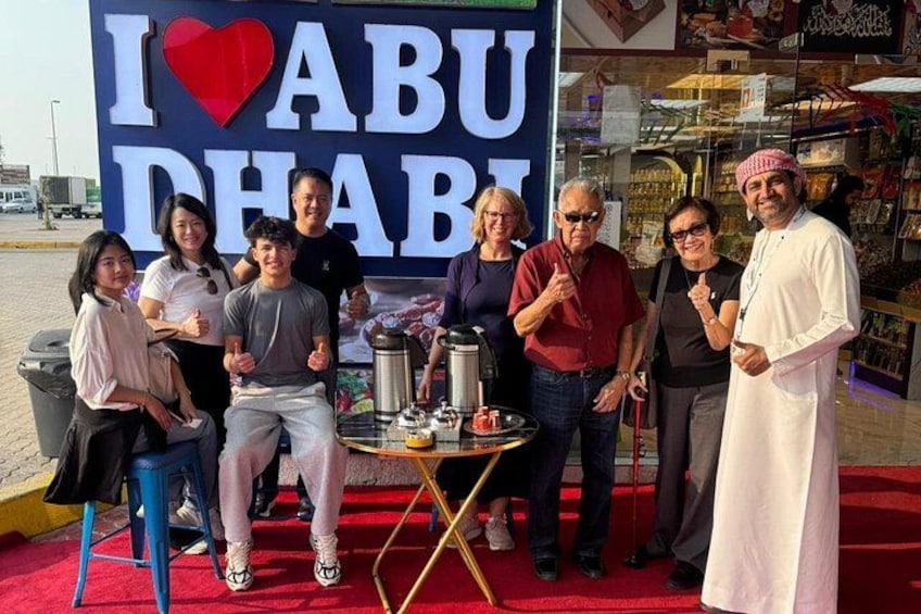 Un grupo de personas posando frente a un cartel que dice 'I ♥ ABU DHABI', una mesa y una alfombra roja. 3