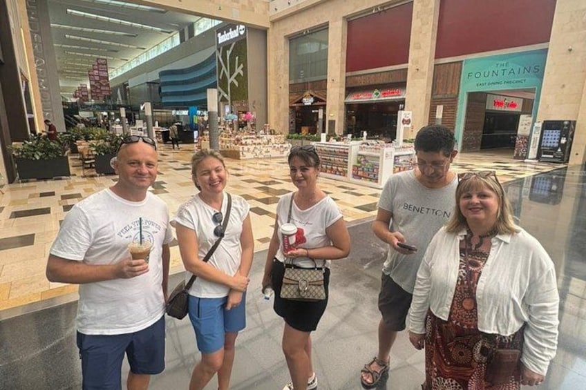 Un grupo de personas en un centro comercial, con tiendas como The Fountains y Benetton al fondo. 2