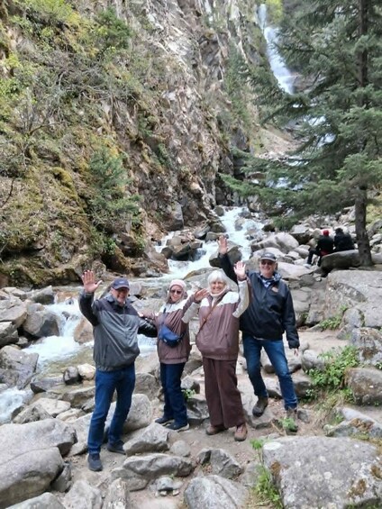 A group of people standing on rocky terrain with a waterfall in the background. 3
