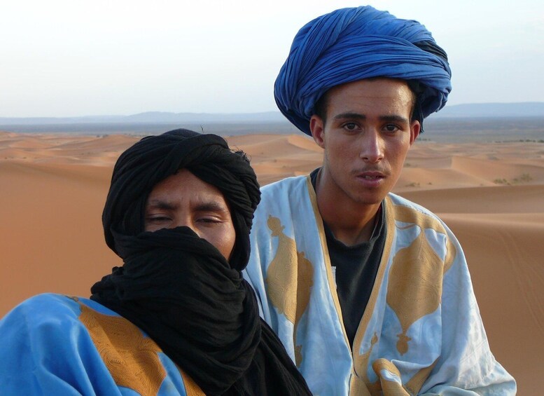 Two individuals in traditional attire with a desert landscape in the background. 1