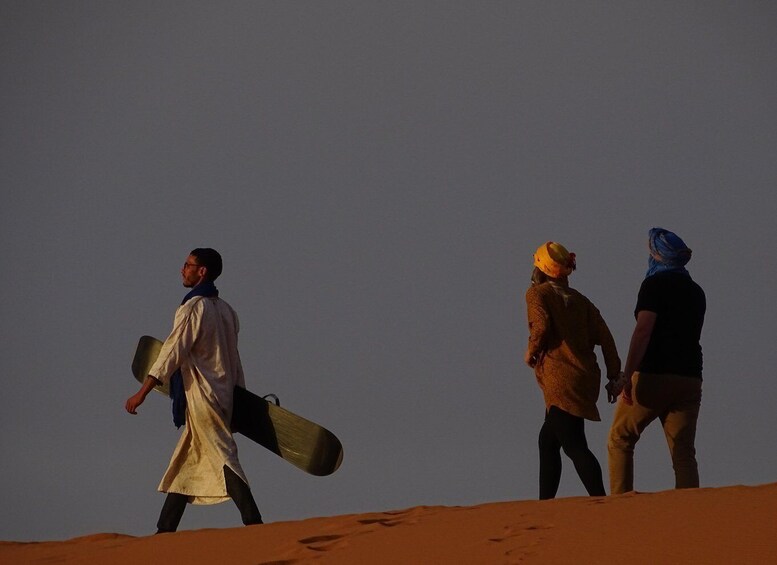 Three people walking across a desert landscape with sand dunes. 3