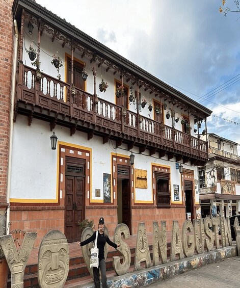A building with ornate balconies and hanging flower baskets, with a sign reading 'SANTA AGUASIA' in the foreground. 3