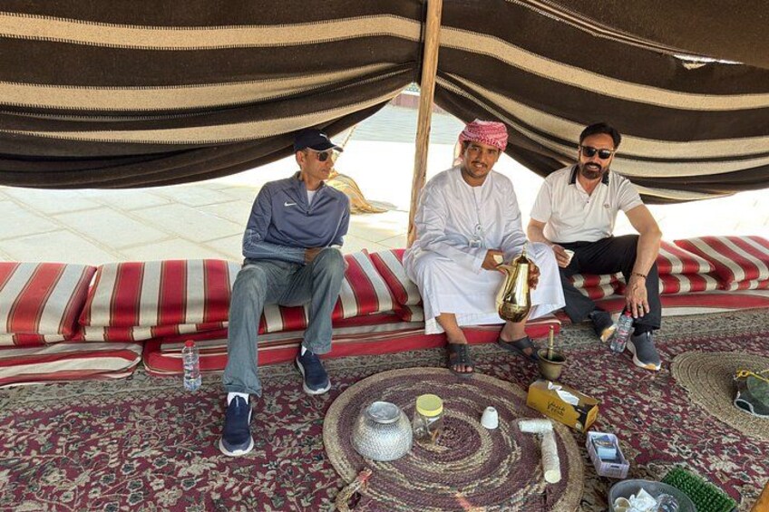 Tre persone sedute su un tappeto decorato sotto una tenda a righe. 2