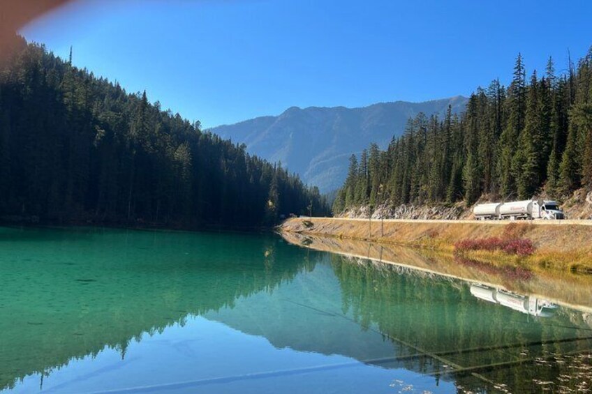 Un lago tranquilo que refleja árboles y montañas, con un camión en la orilla. 5