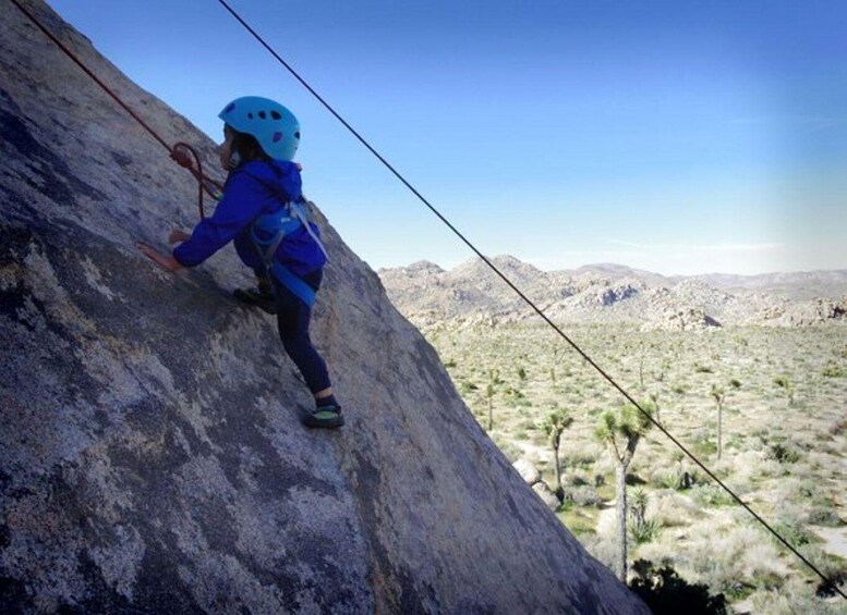 A person climbing a rocky mountain with a clear sky and sparse vegetation in the background. 2