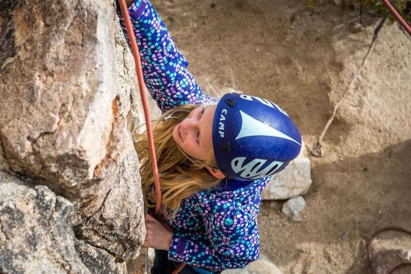 A person climbing a rock with a helmet and a patterned jacket. 4