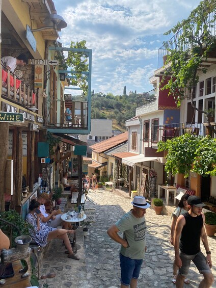 A cobblestone street with shops, outdoor seating, and a person walking. 5