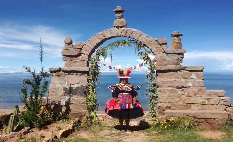 A person in traditional attire standing in front of a stone archway with a view of the sea. 2