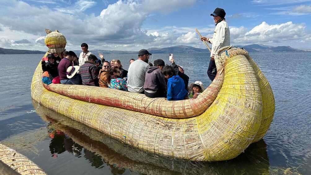 A group of people on a large, intricately woven boat on water with mountains in the background. 1