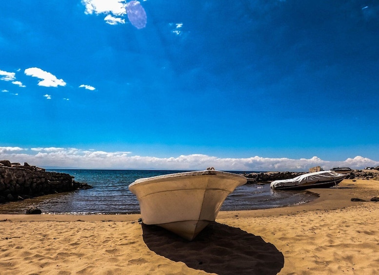 A boat on a sandy beach with a rocky shoreline and a clear blue sky. 3