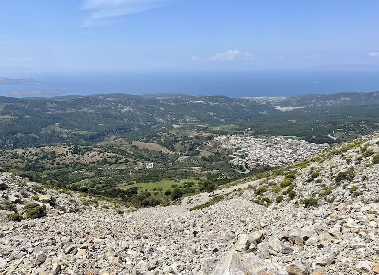 A mountainous landscape with a town nestled in the valley, rocky terrain, and a distant view of the sea. 4