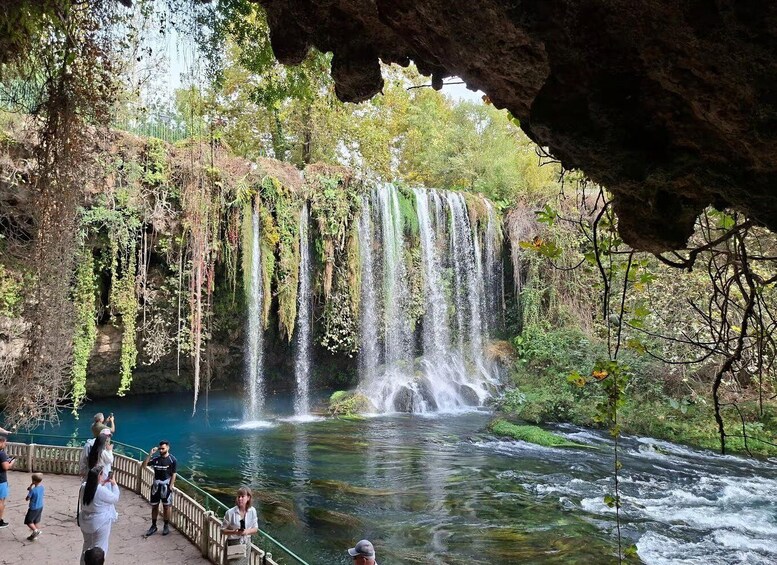 A waterfall cascading into a clear river surrounded by lush greenery and a rocky cave entrance. 3