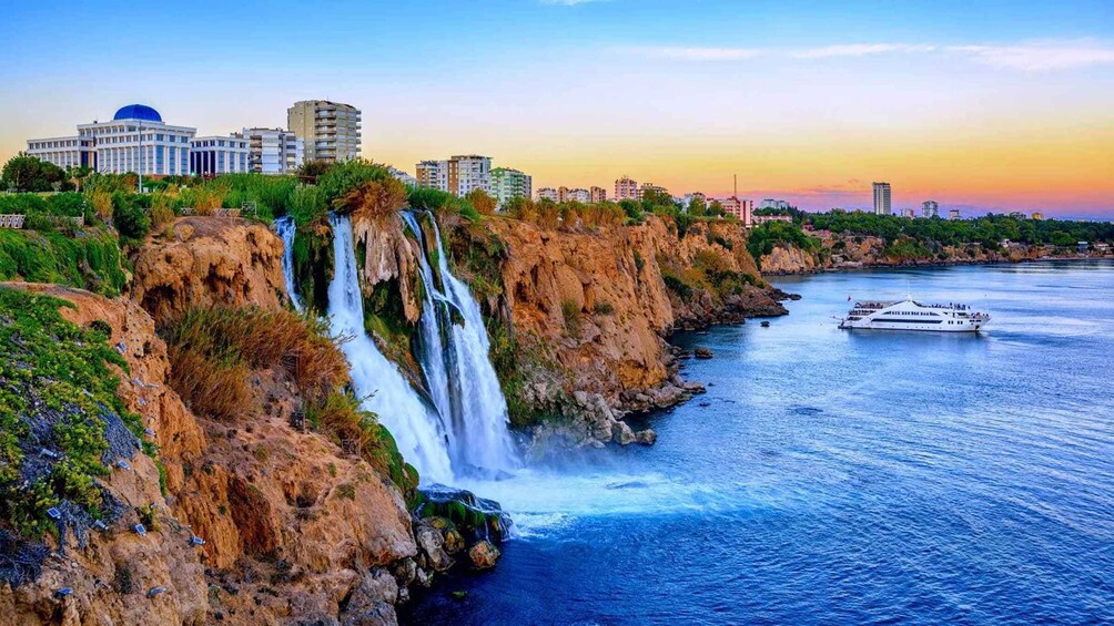 A coastal cityscape with a waterfall, a cruise ship, and modern buildings. 2