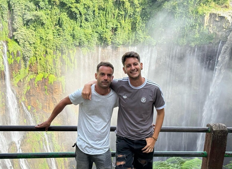 Two people standing by a waterfall with lush greenery in the background. 5