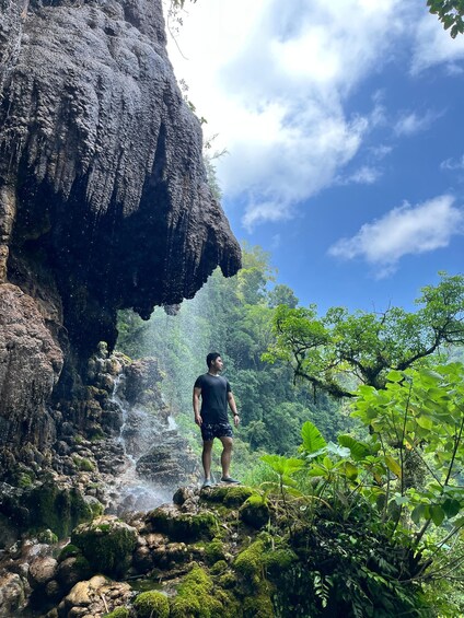 A person standing on a moss-covered rock formation with a waterfall in the background. 2