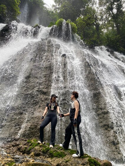 Two people standing on a rocky outcrop with a waterfall in the background. 4