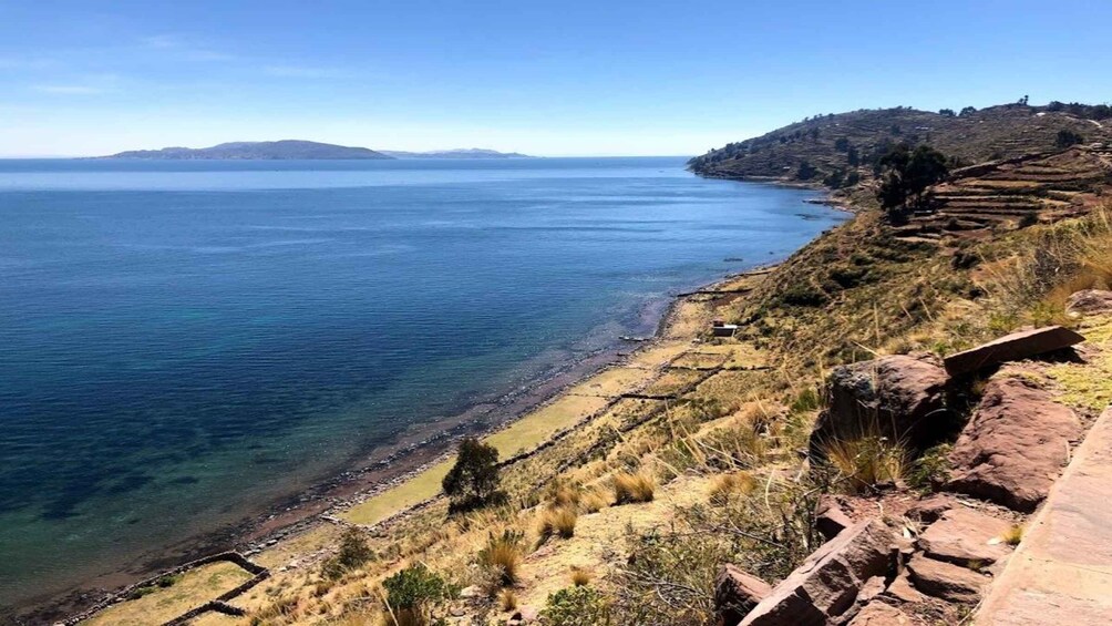 A coastal landscape with terraced fields, a clear blue sea, and distant hills. 3