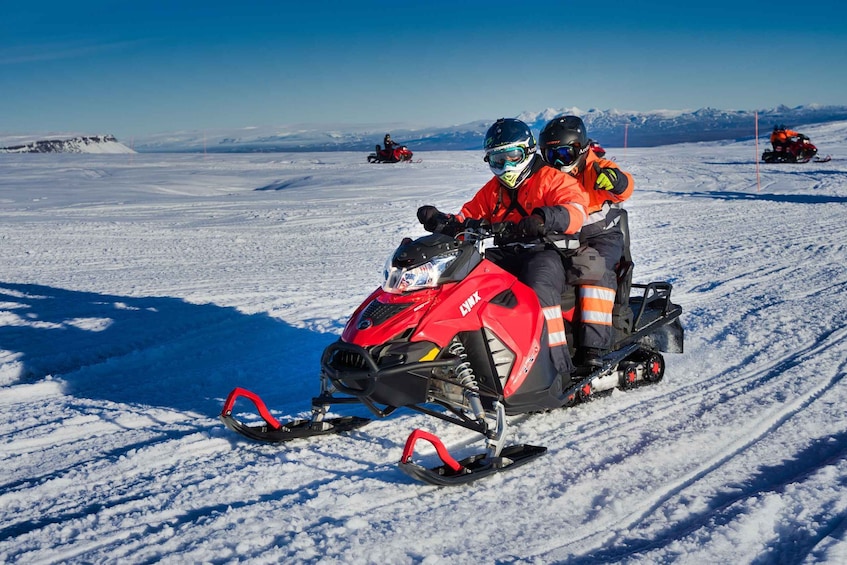 A person riding a red snowmobile on a snowy landscape with mountains in the background. 1