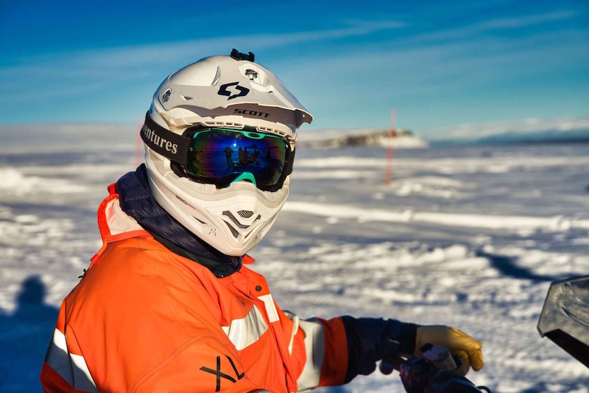 A person in a white helmet and orange jacket, with a snowy landscape and a clear sky in the background. 4
