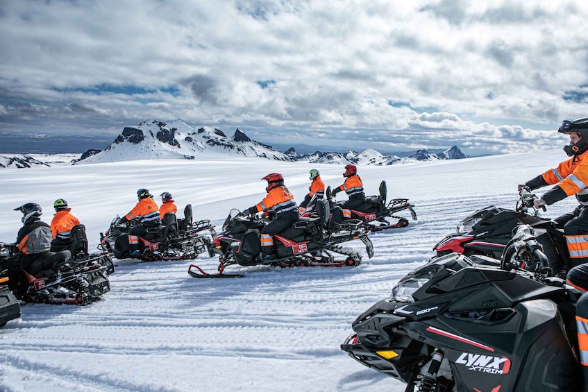 A group of people on snowmobiles in a snowy landscape with mountains in the background. 5