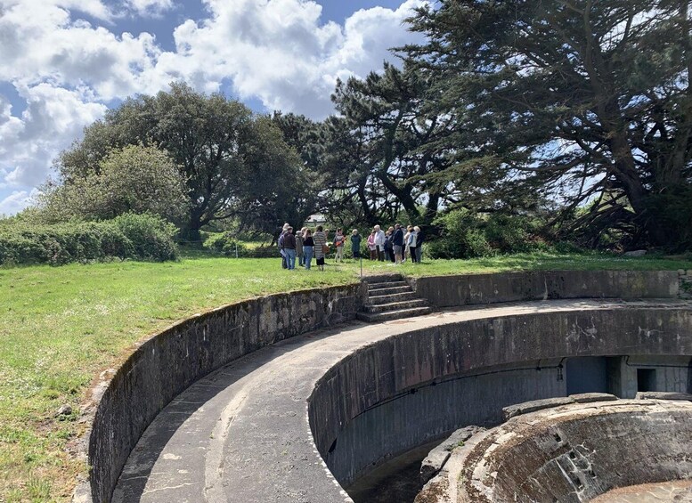 A curved stone structure with people standing on top, surrounded by trees and grass. 5