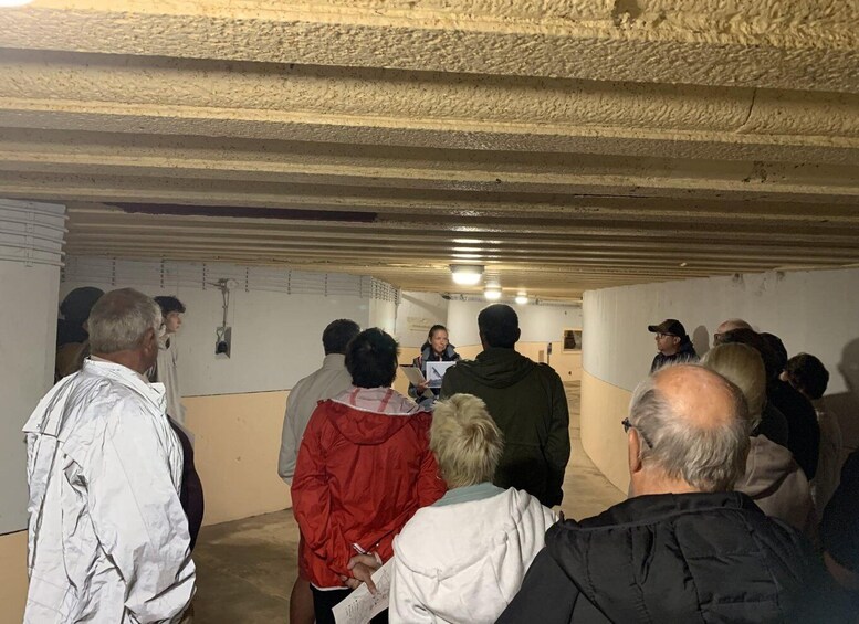 A group of people gathered in an underground room with concrete walls and a sloped ceiling. 3