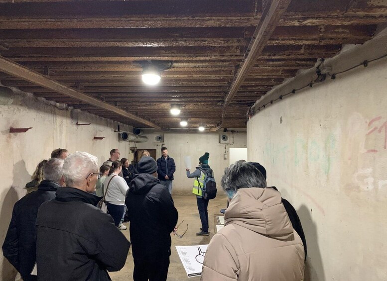 A group of people in a dimly lit, rustic room with wooden beams on the ceiling and graffiti on the walls. 4