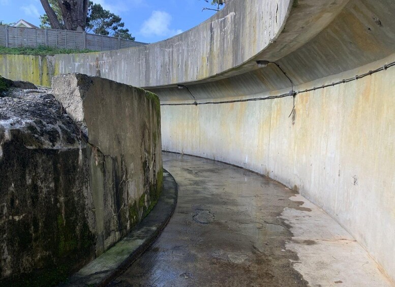 A curved concrete structure with a wet floor, surrounded by a fence and trees. 2