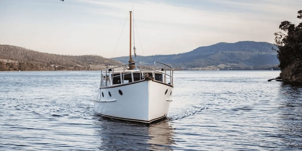A white boat on calm water with a forested shoreline and hills in the background. 1