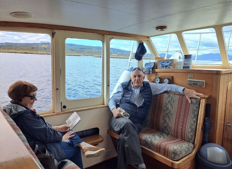 A boat interior with two people seated, a steering wheel, and a view of a lake. 5