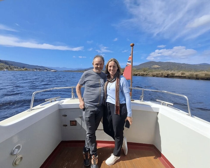 A couple on a boat with a flag, water, and hills in the background. 2