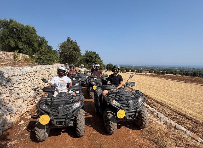 A group of people on ATVs on a dirt path with a stone wall on one side and a field on the other. 2