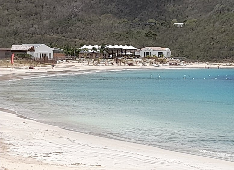 A beach with clear water, a sandy shore, and a row of buildings in the background. 4