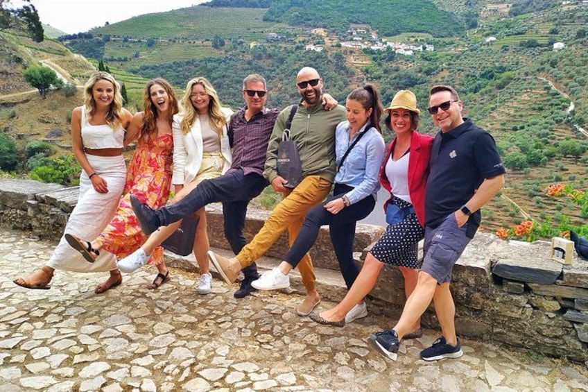 Un grupo de personas posando sobre un muro de piedra con un valle pintoresco al fondo. 2